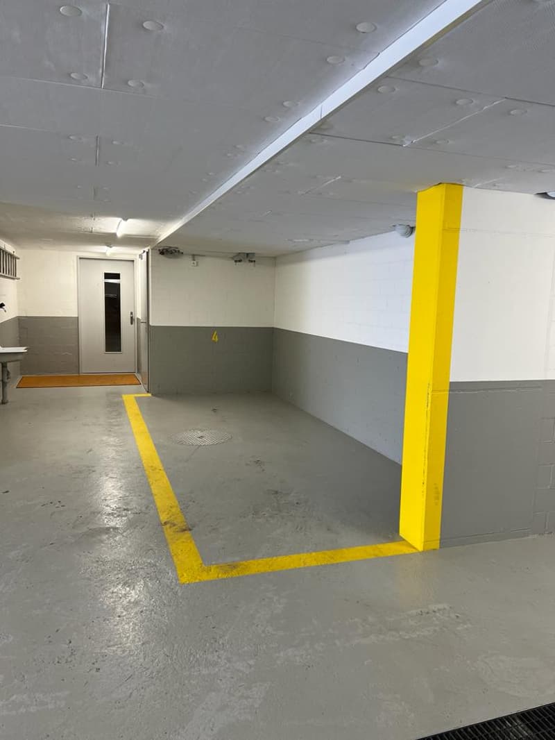 Empty parking space with yellow markings, concrete floor, gray walls, yellow pole, and a white door.