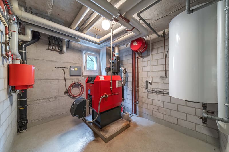 Red boilers, white water tank, exposed pipes, grey brick wall, small window