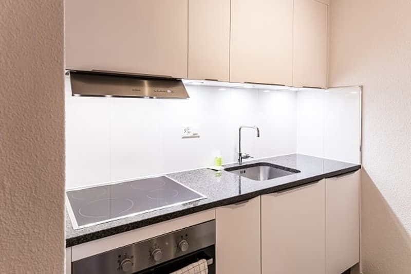 Modern kitchen with white cabinets, stainless steel appliances including a dishwasher, and a granite countertop with a sink and faucet.