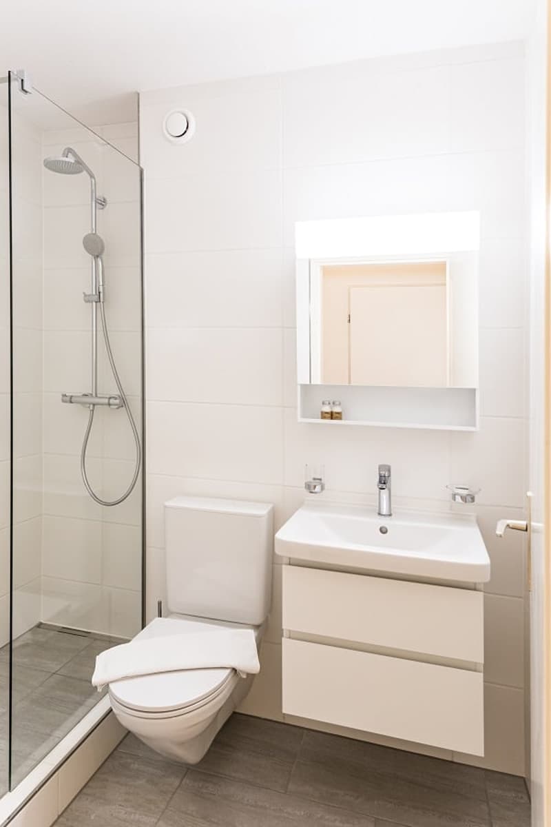 Modern bathroom with white walls, tiled floor, shower enclosure, vanity unit with sink, and toilet
