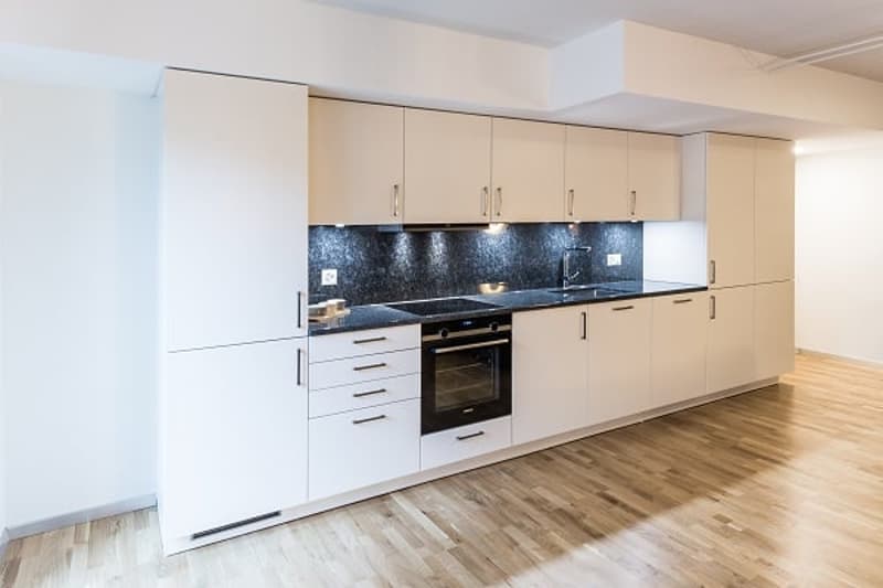 Spacious modern kitchen with white cabinets, black backsplash, built-in oven and dishwasher, hardwood flooring