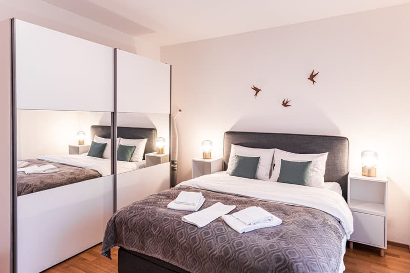 modern bedroom, double bed, grey bedspread, white bedding, bedside tables, lamps, mirrored wardrobe