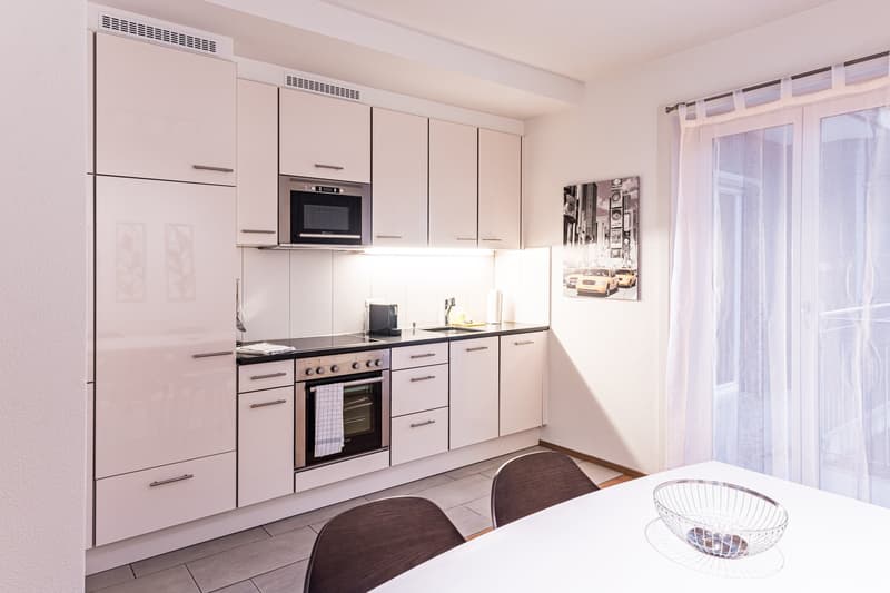modern kitchen with white cabinets, black countertops, stainless steel appliances, large windows