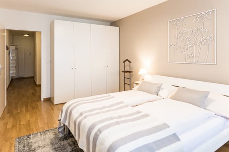 Double bed, grey and white duvet, white headboard, white wardrobe, picture frame, night stand, lamp