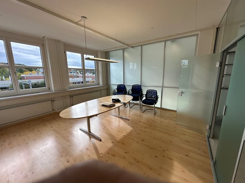 Spacious office space with large windows, hardwood floors, a conference table with chairs, and a glass partition wall.