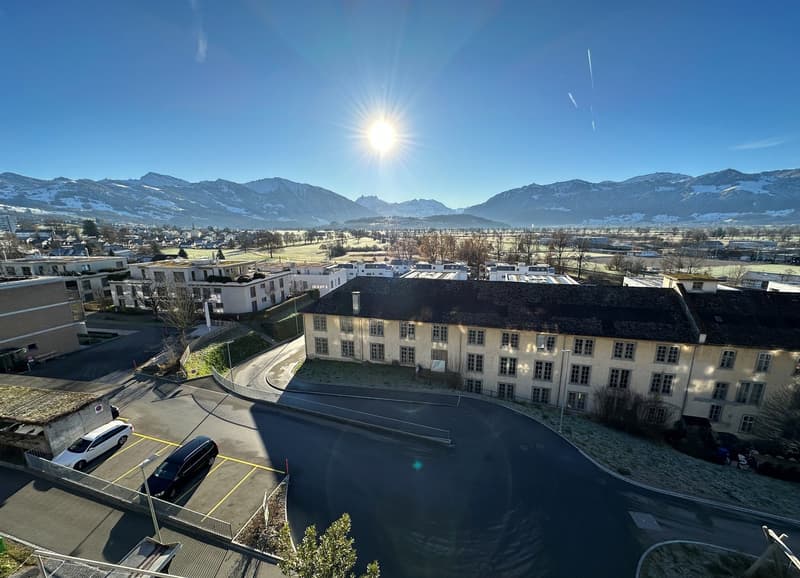 aerial view of a white house with a garage, parking lot, and snowy mountains in the background