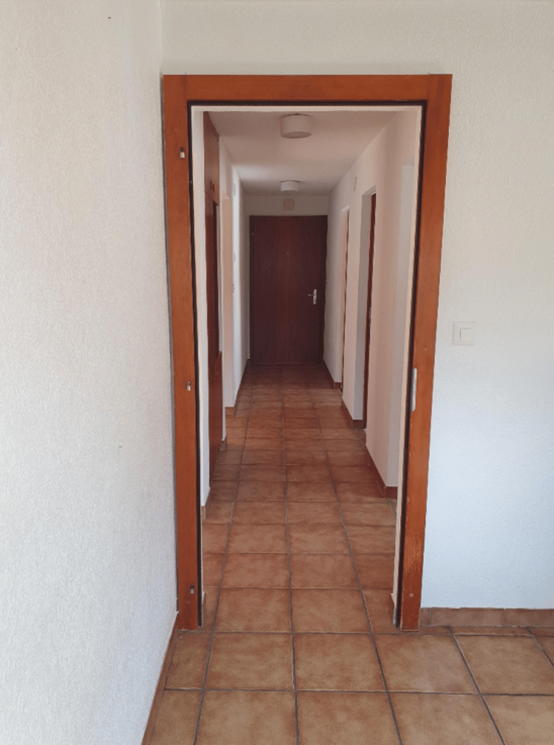 The image shows a hallway with a tiled floor and wooden door frames. The hallway appears to be long and leads to other rooms or areas of the property.