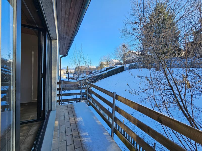 Wooden balcony with glass railings, tiled floor, snowy slope view, clear blue sky
