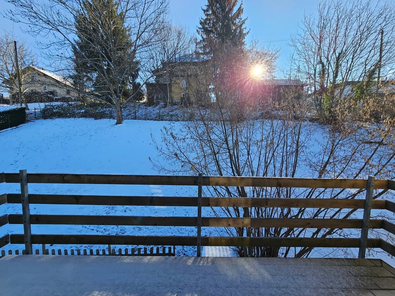 Outdoor view of a snowy backyard with a wooden fence and a building in the background