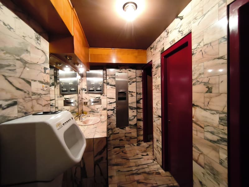 Marble-tiled walls, wooden cabinets, urinal, and a washing machine