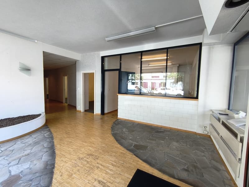 Large open space with hardwood floors, stone accent wall, and glass windows overlooking the exterior. There appears to be a fireplace or other heating element in the corner of the room.
