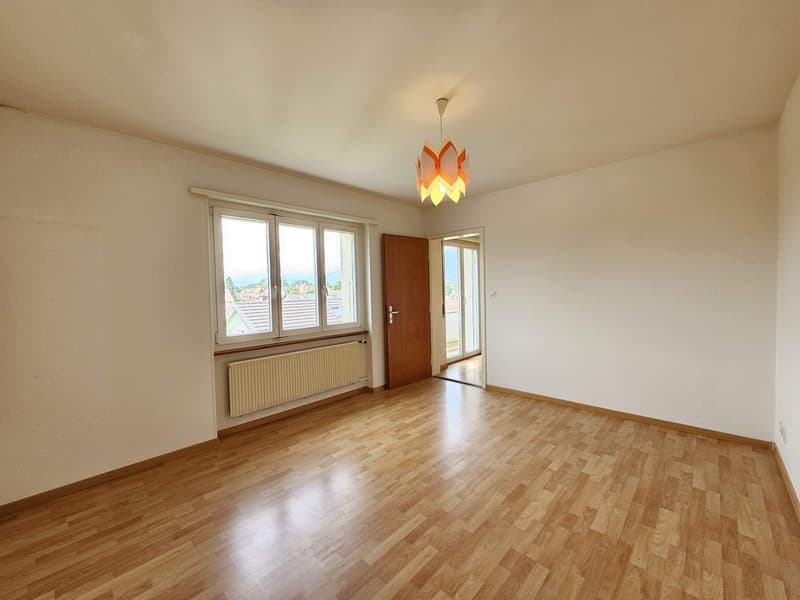 Spacious living room with hardwood flooring, large windows providing natural light, and a decorative pendant light fixture.