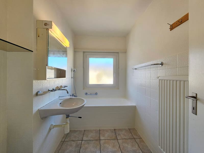 Bathroom with white walls, white bathtub, white sink, mirror, towel rack