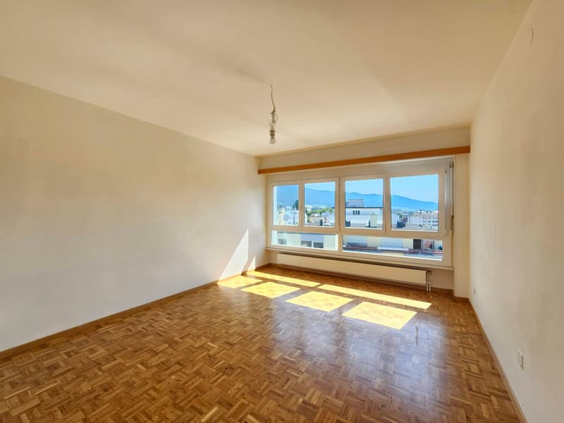 Spacious living room with large windows offering a scenic view, hardwood parquet flooring, and a simple, minimalist decor.
