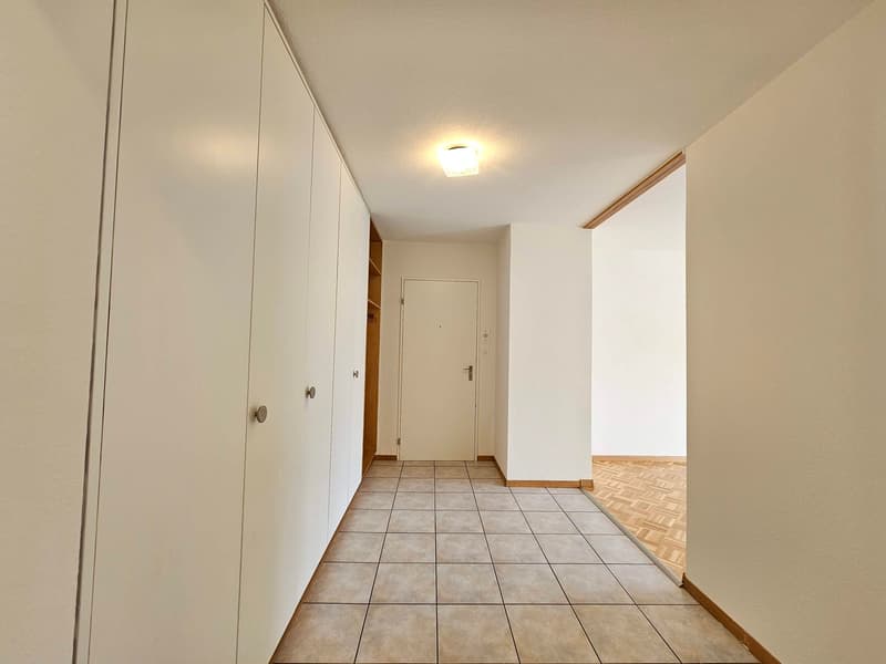 Empty hallway with tile flooring, white walls, cabinets, closed white door, and recessed ceiling light