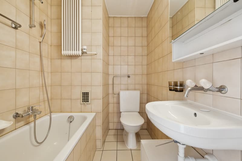Tiled bathroom with bathtub, toilet, sink, and radiator