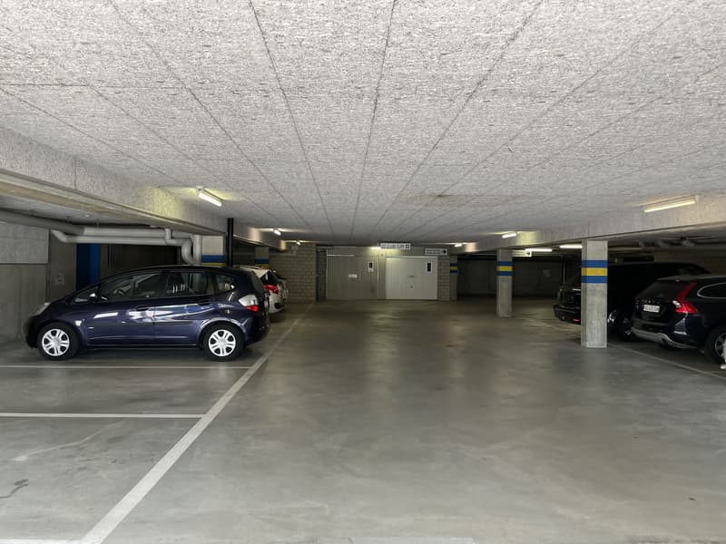 Underground parking garage with concrete floor, parked cars, and storage rooms