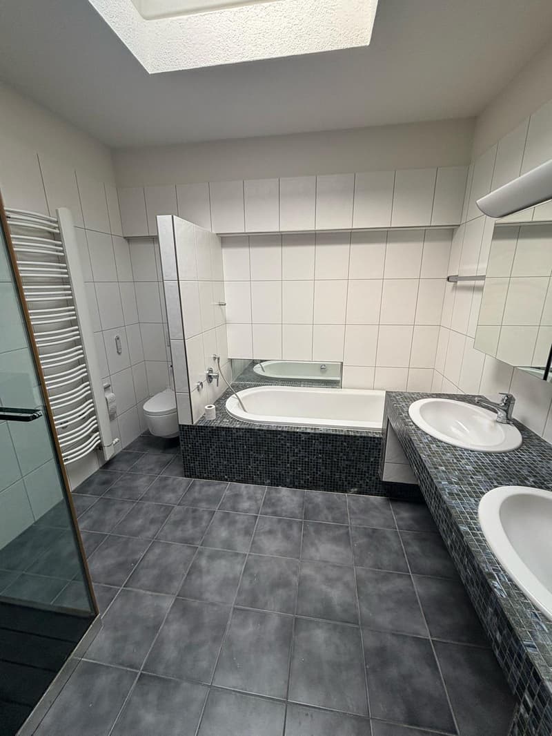 Spacious bathroom with white walls, gray tile flooring, a bathtub, a shower, and a vanity with a sink
