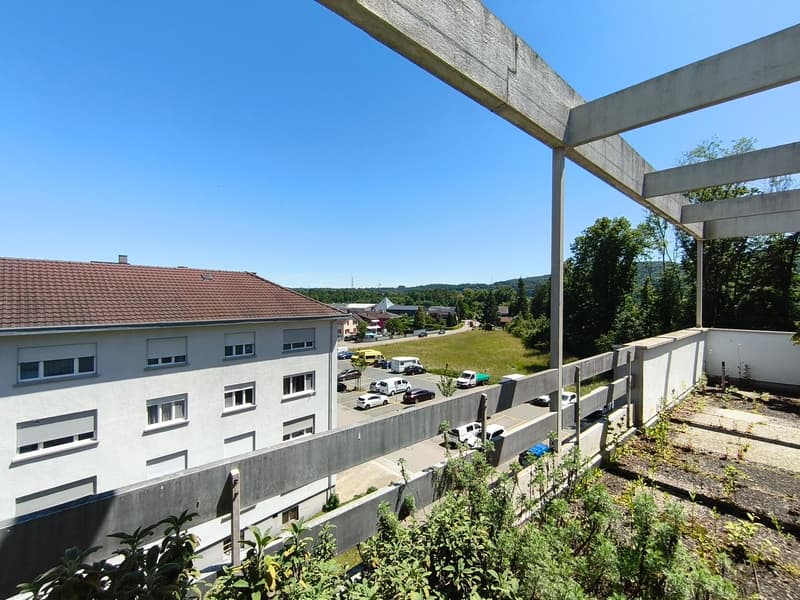 Multi-story residential building with a balcony or terrace, surrounded by trees and greenery. The building has a view of the surrounding landscape and nearby structures.