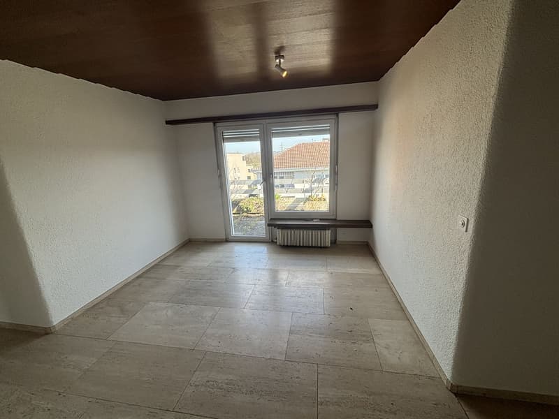 Empty room with white walls, tile flooring, and a window overlooking the exterior. The room has a dark-colored ceiling with a single light fixture.