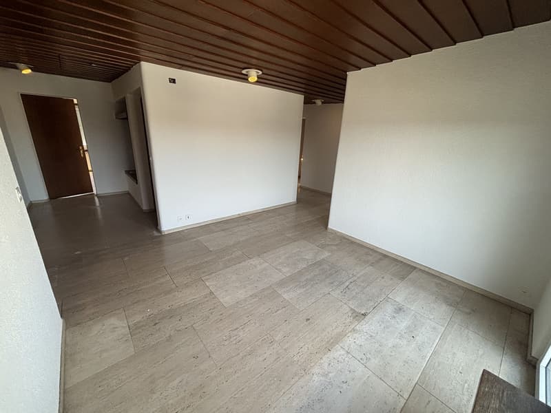 The image shows a spacious room with a wooden ceiling and tile flooring. The walls are painted in a neutral color, and the room appears to be empty, with no furniture or decor visible.