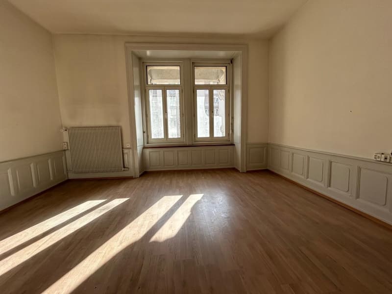 Spacious room with hardwood floors, large windows, and paneled walls. The room appears to be empty, with natural light streaming in through the windows.