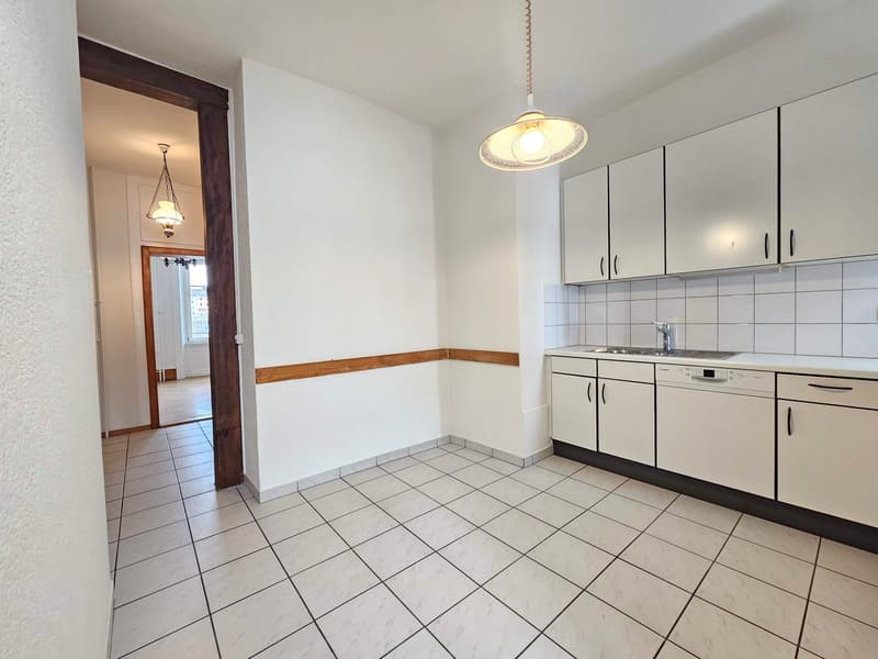 Empty kitchen with white tiles and cupboards, sink, dishwasher, and lamps