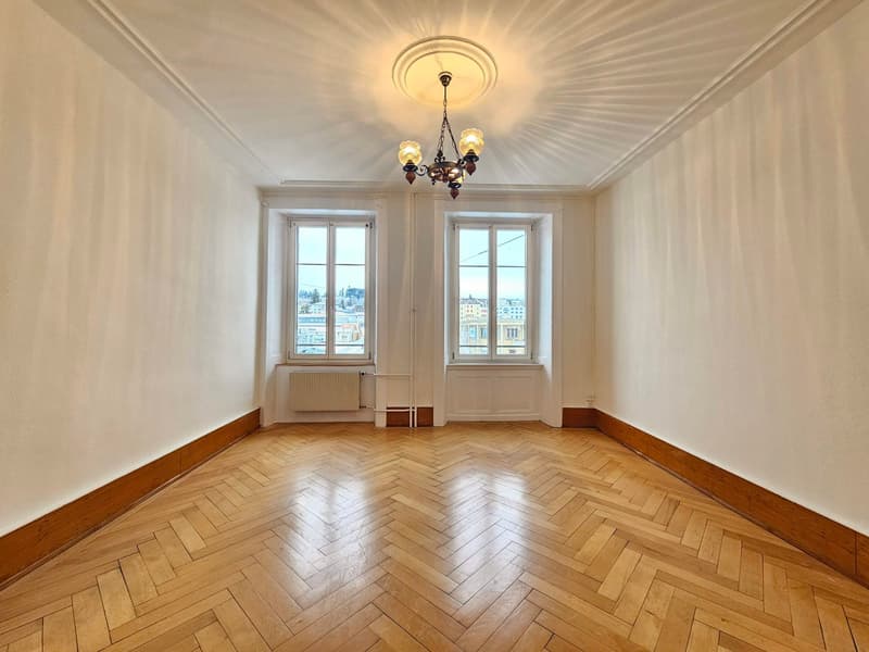 Empty room, parquet floor, chandelier, two windows, radiator