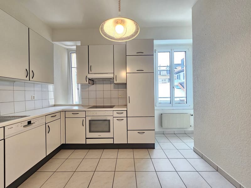 Modern kitchen with white cabinetry, tile flooring, built-in appliances including an oven and dishwasher, and ample counter space.