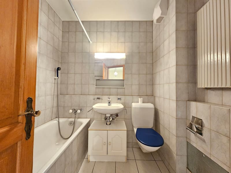 white bathtub, white sink with metal faucet, white toilet, small wooden cabinet, silver showerhead, tiled walls
