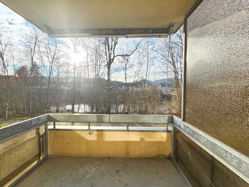A balcony with metal railings, a yellow concrete wall, and a view of trees and a body of water.