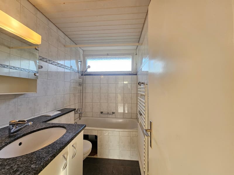 Bathroom with tiled walls, bathtub, sink with mirror, toilet, and towel rack.