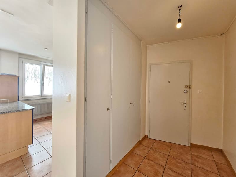 empty room with tile flooring, white walls, two doors, window with radiator, corner cabinet, lamp