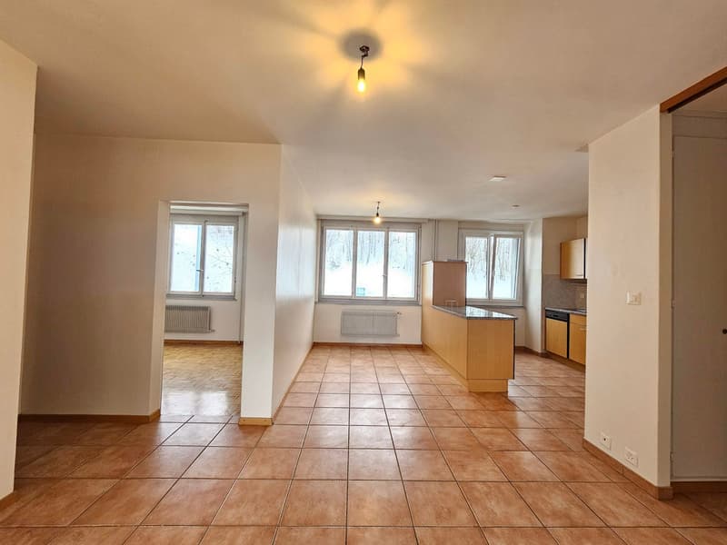 Empty room with brown tile flooring, large windows, open door, kitchen island, built-in appliances