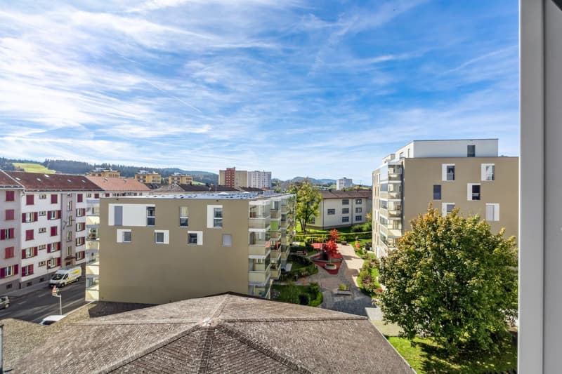 View from a high floor, balcony, garden area, multiple buildings in the area, clear blue sky