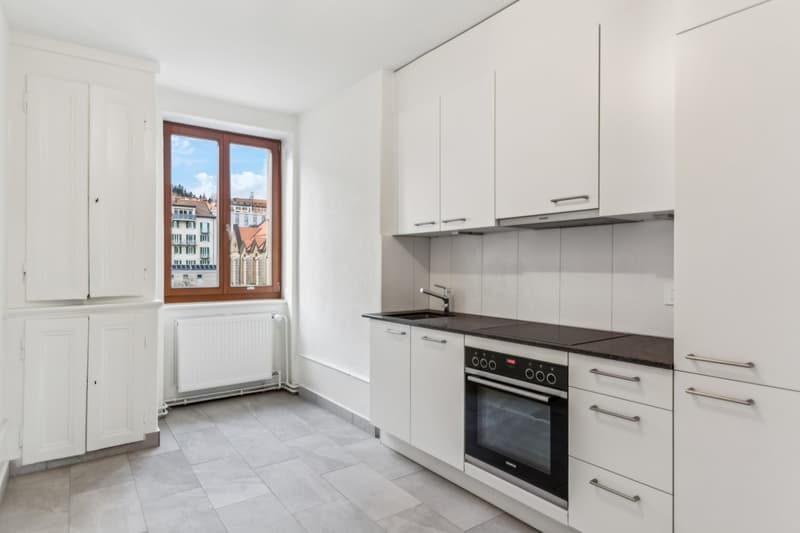 modern white kitchen, dishwasher, built-in oven, tiled floor, white cabinets, black granite countertop, radiator