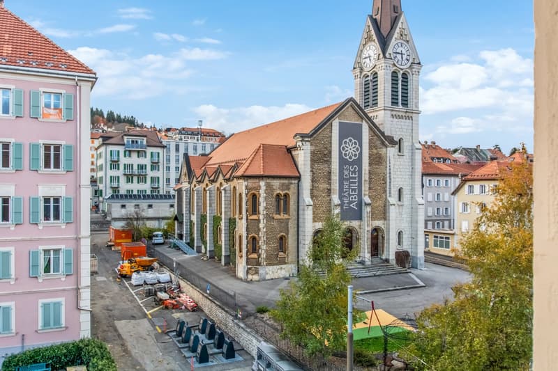 Church with brown roof and white steeple with clock, surrounded by construction materials and a street.
