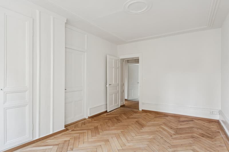 empty room with wooden floor, white walls, doors, and electrical outlets