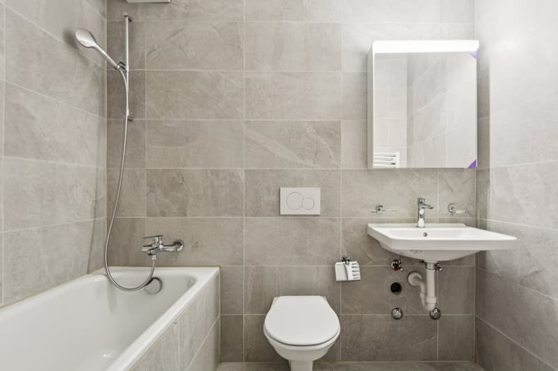 Bathtub with shower, white tiles, white sink, toilet, mirror, sink roll