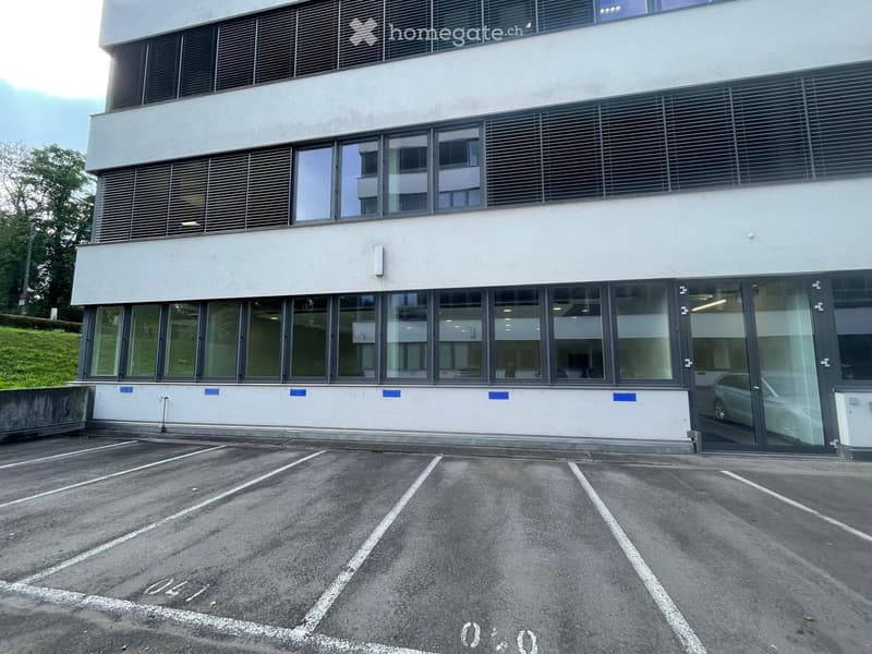 large glass windows, white concrete exterior, two parking spaces in front, entrance with double doors