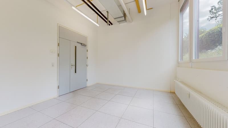An empty room with tiled flooring, white walls, white door, and a radiator on the right side. There are windows and a white door, and a white ceiling with a light fixture