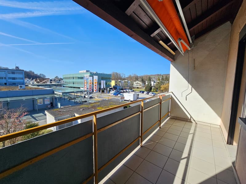 Balcony with tiled floor, metal railing, view of a parking lot and buildings