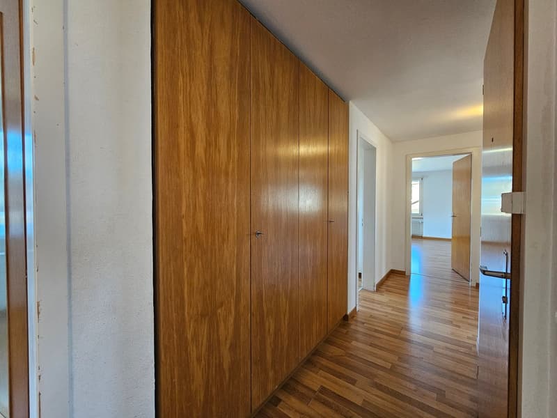 Empty hallway with wooden floor, wooden built-in wardrobes, white walls, open doors