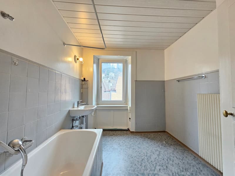 Bathroom features a bathtub, sink, window, radiator, and tiled walls