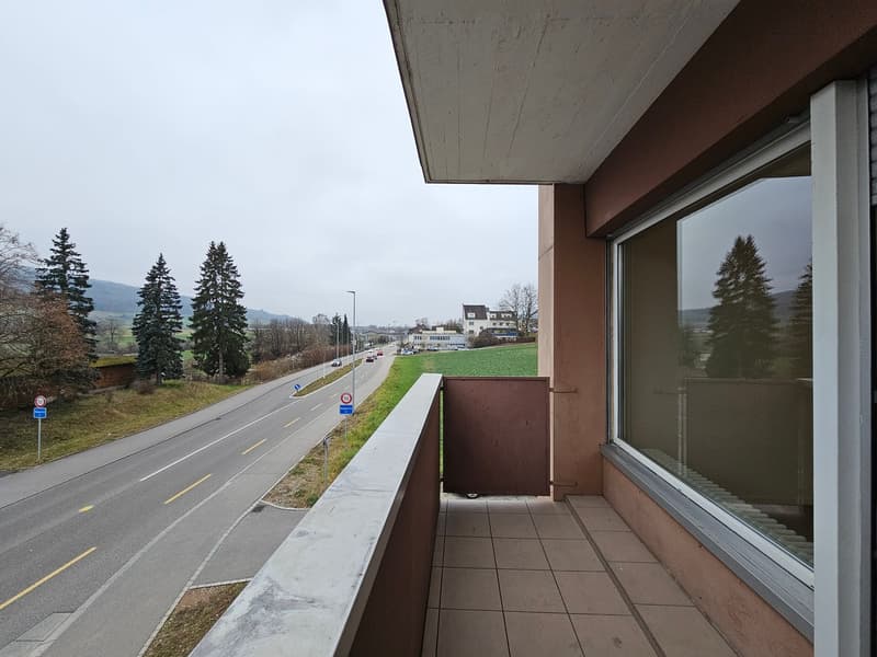 A balcony with a tiled floor, a brown rail, and a view of a road with street signs and trees