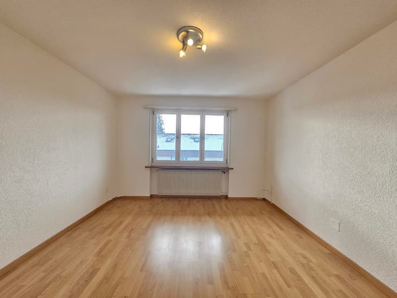 Room with wooden floor, white walls, single window, radiator below the window