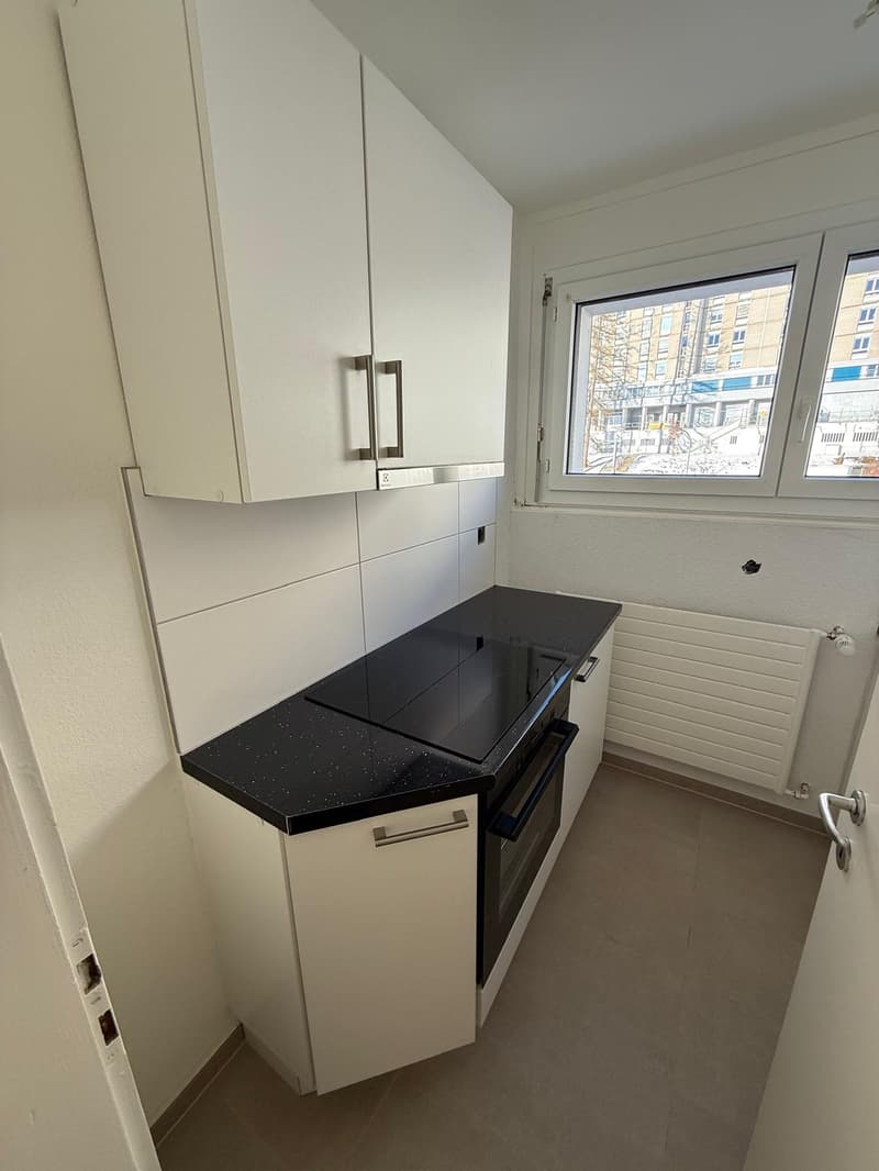 modern kitchen with white cabinets, black countertop, electric stove, integrated dishwasher, white floor, window