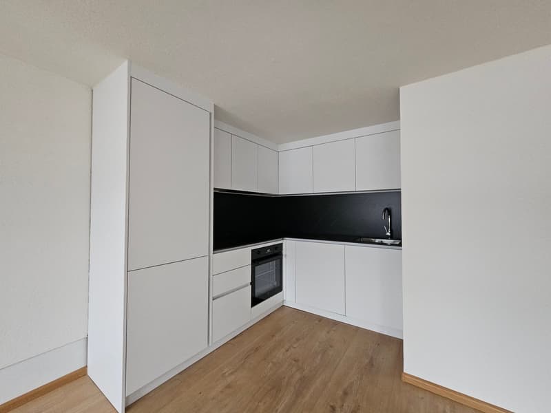 minimalist kitchen with oven, sink, wooden floor, white cabinets, black countertops