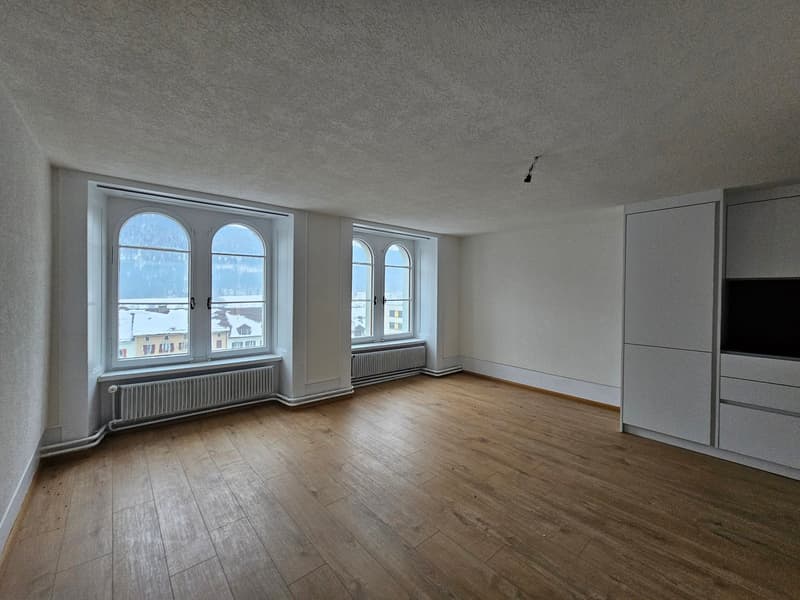 large room, wooden floors, three large windows, white walls, white cabinets, radiators under windows