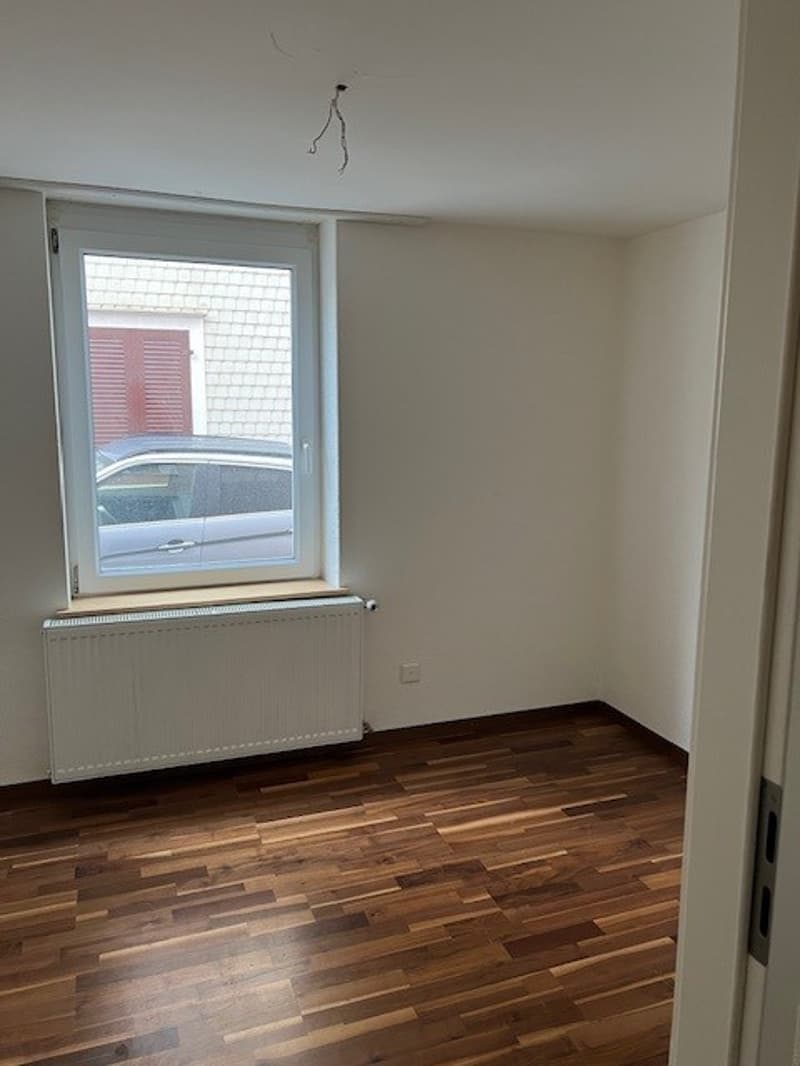 empty room, white walls, wooden floor, white radiator, window with a view to the street